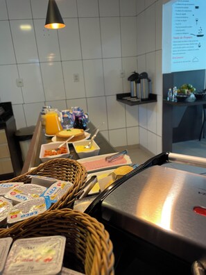 A breakfast buffet setup with various food items, a refrigerator, and a menu board. - Pousada Mel e Mar (Penha)