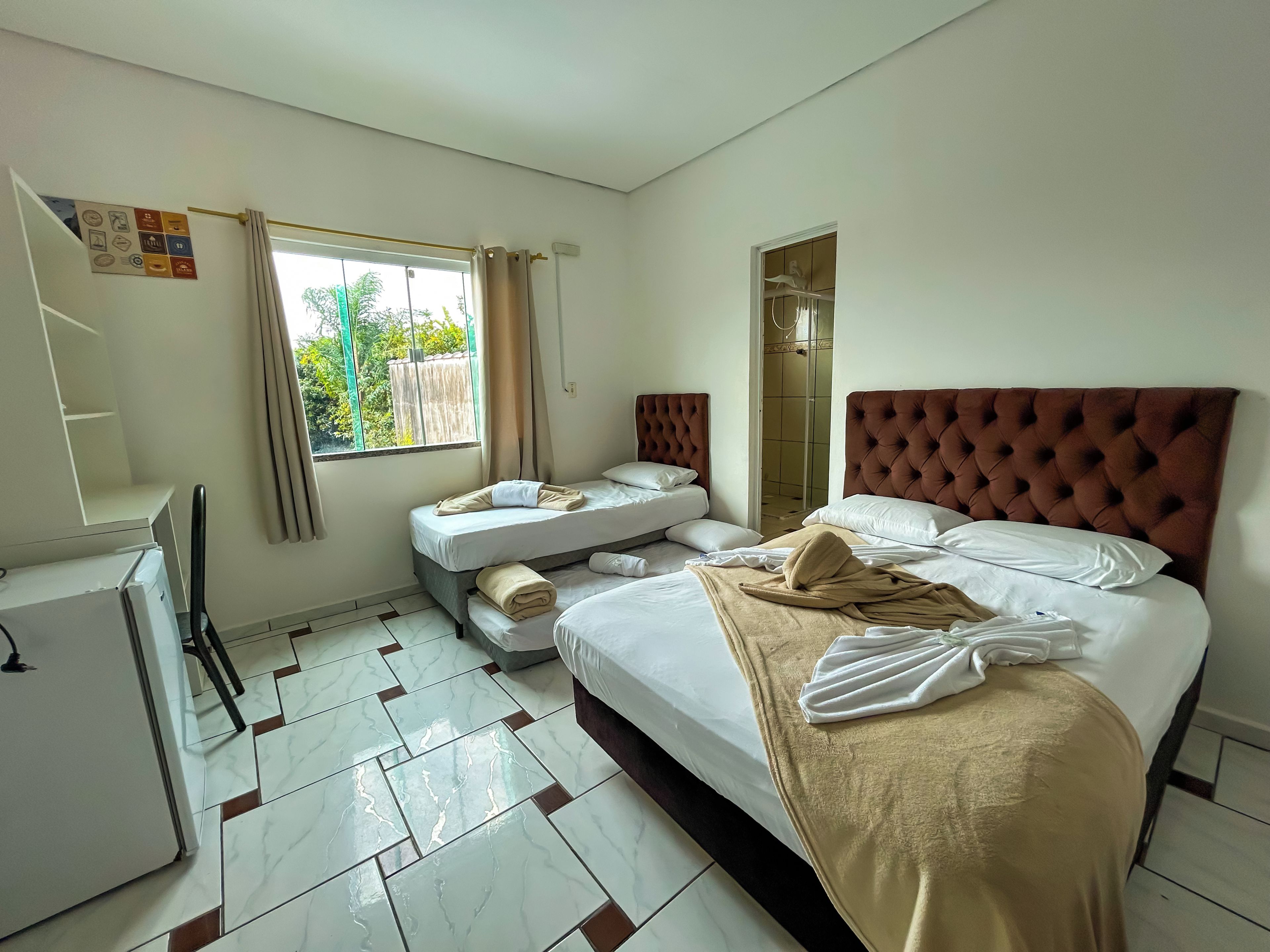 A hotel room with a bed, a small desk, a refrigerator, and a window with curtains.