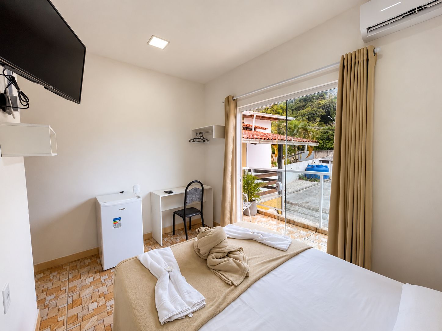A hotel room with a bed, a desk, a chair, a television, and a view of the outside.