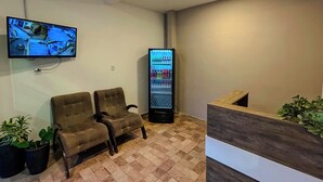 Zona d'acollida amb taulell d'informació, dues cadires, un televisor penjat a la paret i una màquina expenedora.
