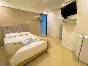 A hotel room with a bed, a television mounted on the wall, a door, and a small white cabinet. - Pousada Mel e Mar (Penha)