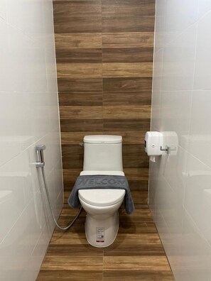 A compact bathroom with a white toilet, a shower, and a toilet paper dispenser. - Pimann Place Hotel (Chiang Rai)