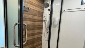 A modern bathroom with a wooden floor, a shower with a handheld showerhead, and a glass door.