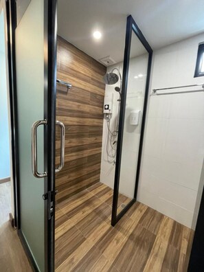 A modern bathroom with a wooden floor, a shower with a handheld showerhead, and a glass door. - Pimann Place Hotel (Chiang Rai)