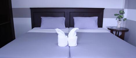 A neatly made bed with two towels folded in the center, a dark headboard, and a small bedside table with a plant.