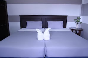 A neatly made bed with two towels folded in the center, a dark headboard, and a small bedside table with a plant. - Pimann Place Hotel (Chiang Rai)