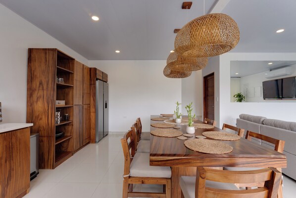 A modern kitchen with wooden cabinetry, a dining table with placemats, and a hanging woven light fixture.