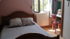 A bedroom with a wooden bed, a window with curtains, a radiator, and a desk with a chair. - La Chapelle (Teloché)