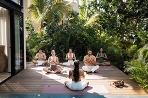 A group of people meditating on yoga mats in an outdoor setting with lush greenery and a wooden deck. - Trobbu Boutique Collection Riviera Maya - All Inclusive (Tulum)