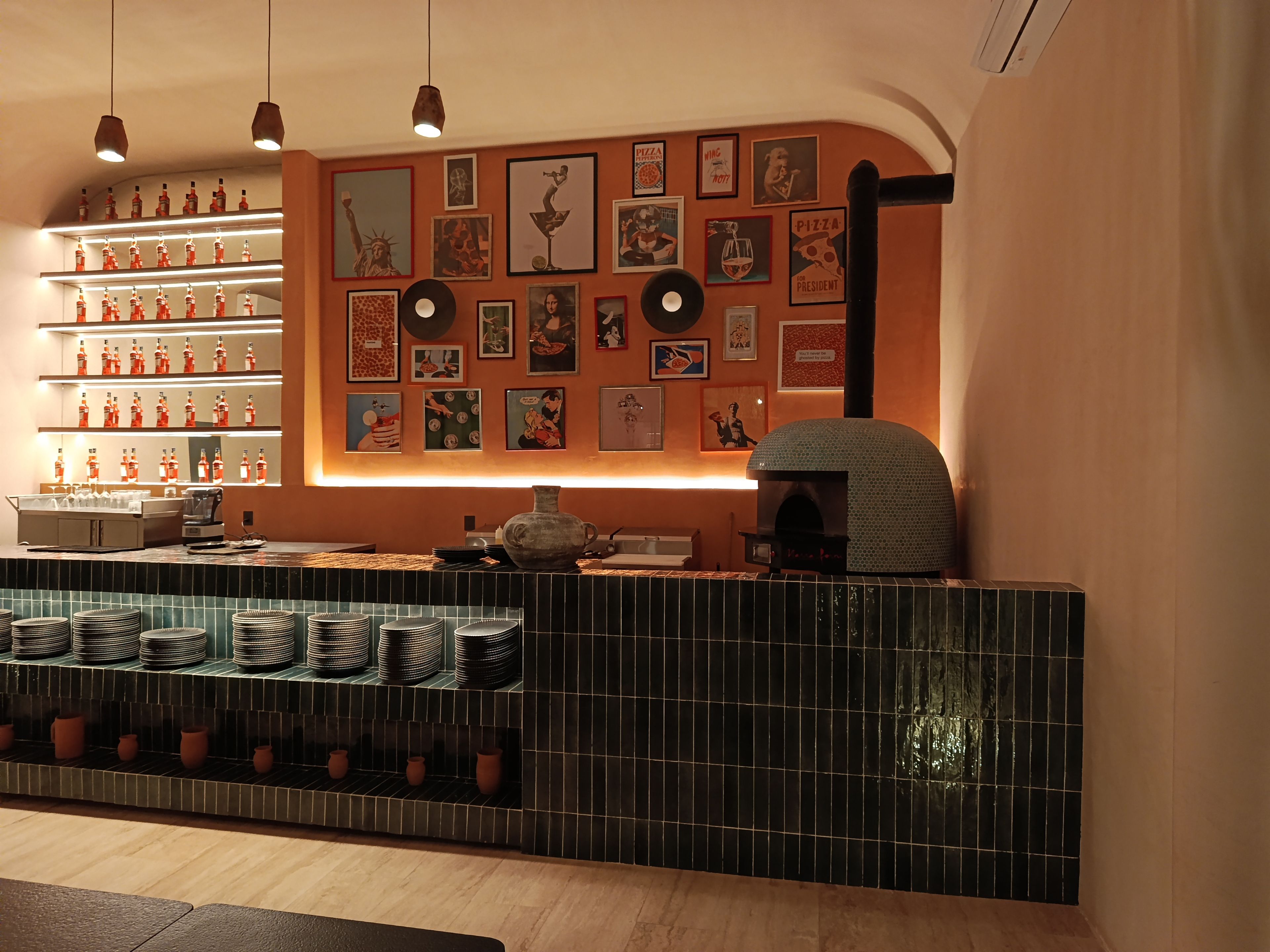 A bar area with a counter, shelves with bottles, and a pizza oven.