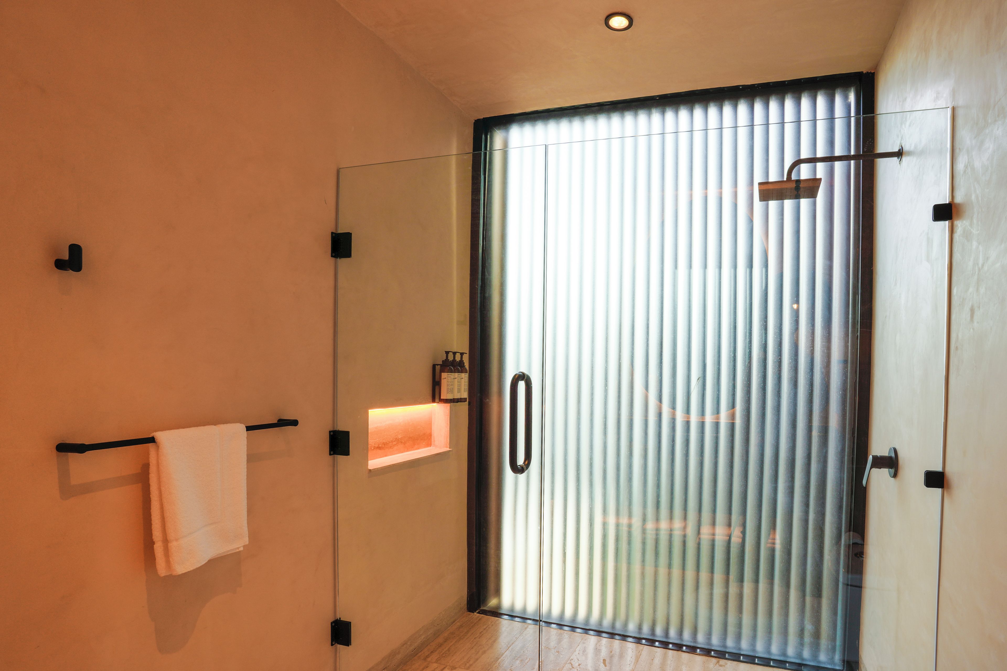 Een moderne badkamer met een douchecabine van glas, een handdoekrek en een klein plankje met toiletartikelen.