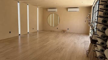 A spacious room with wooden flooring, a round mirror, and air conditioning units.