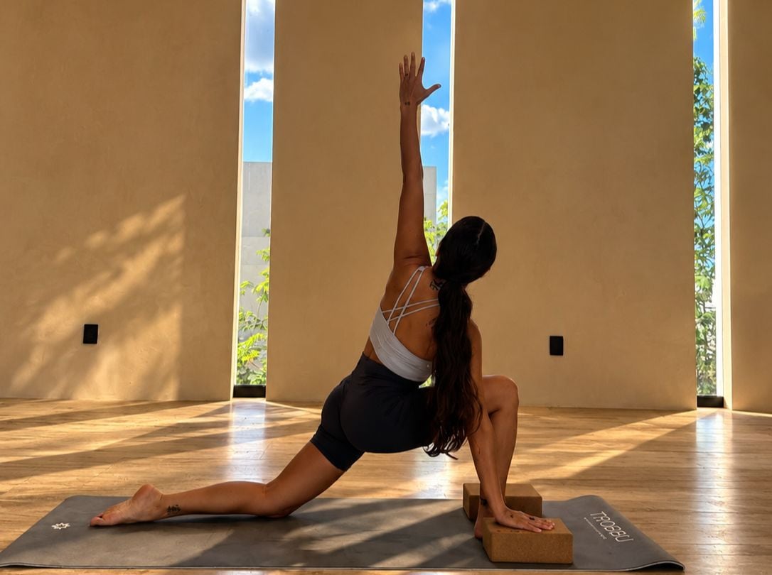 A person performing a yoga pose on a mat in a room with large windows and wooden flooring.