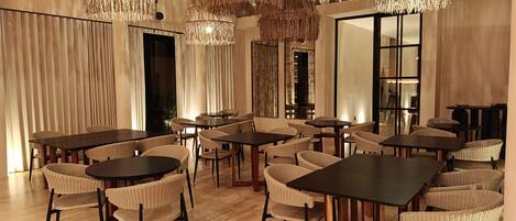 A spacious dining area with multiple tables and wicker chairs, large hanging chandeliers, and a modern interior design.