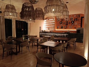 A restaurant with wicker chairs, tables, hanging chandeliers, and a bar area with shelves of bottles. - Trobbu Boutique Collection Riviera Maya - All Inclusive (Tulum)