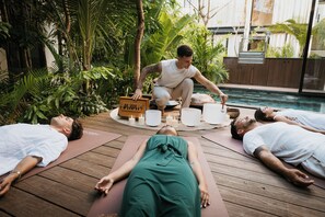 A group of people lying on yoga mats in a wooden deck area with a pool in the background. - Trobbu Boutique Collection Riviera Maya - All Inclusive (Tulum)