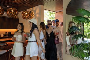 A group of people in a modern interior with wooden ceiling slats, a bar area with a coffee machine, and a dining space with a table and chairs. - Trobbu Boutique Collection Riviera Maya - All Inclusive (Tulum)