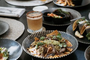 Et spisebord med forskellige retter, herunder en tallerken med nachos, et glas drik og andre spiser.