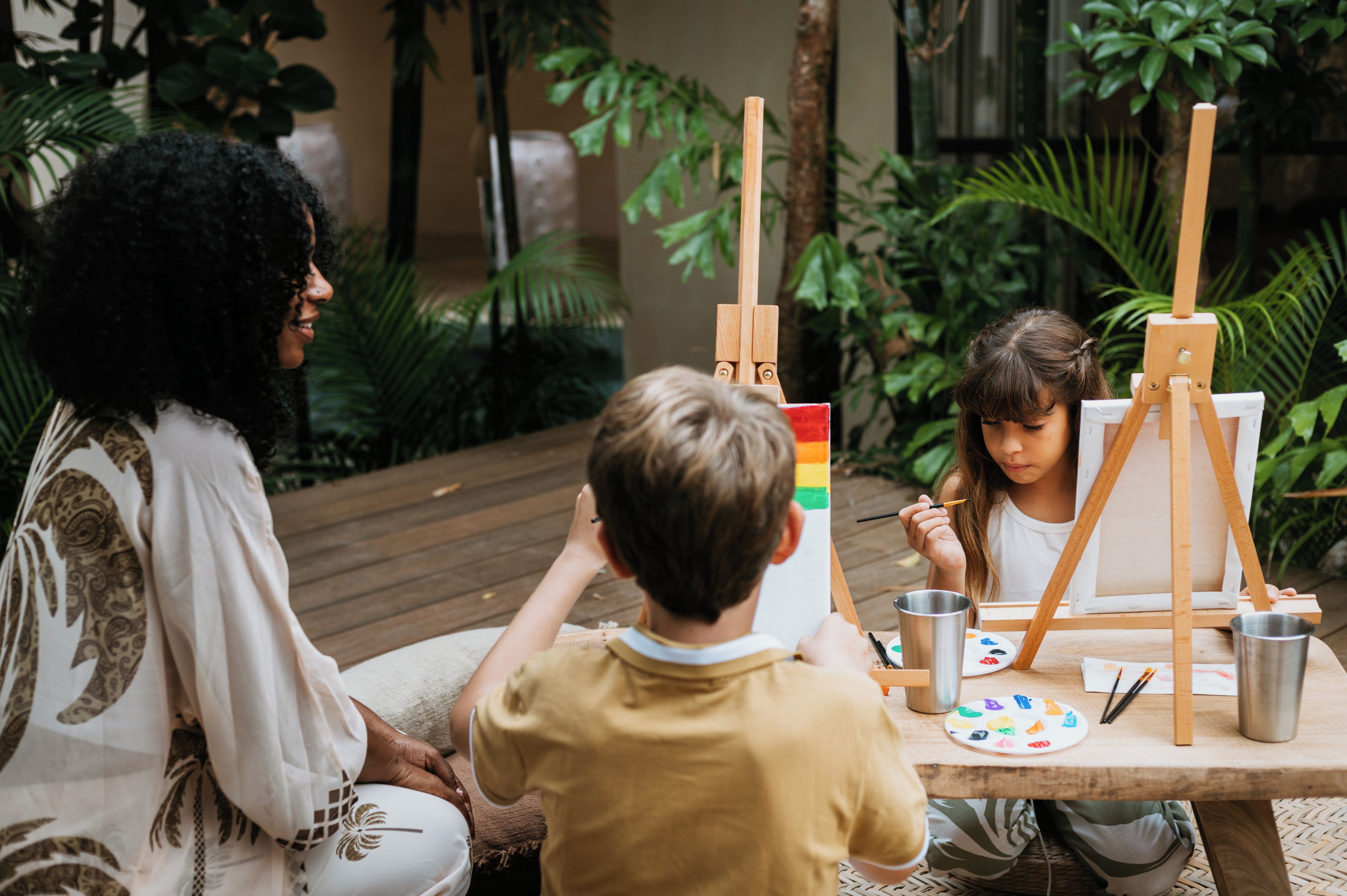 A group of people painting outdoors with easels and paint cups on a table.