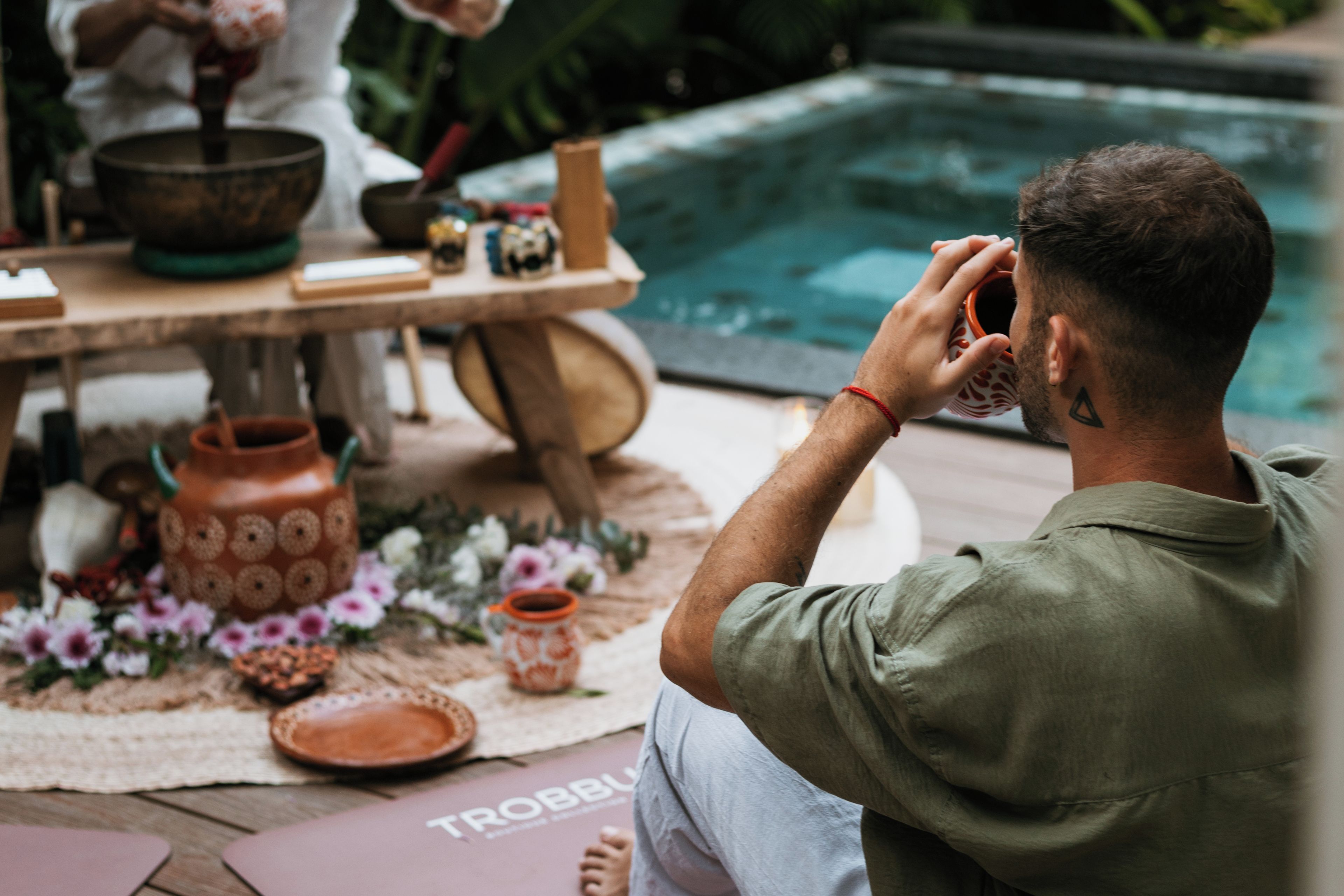 A person sitting by a pool with a table of cooking utensils and a bowl.