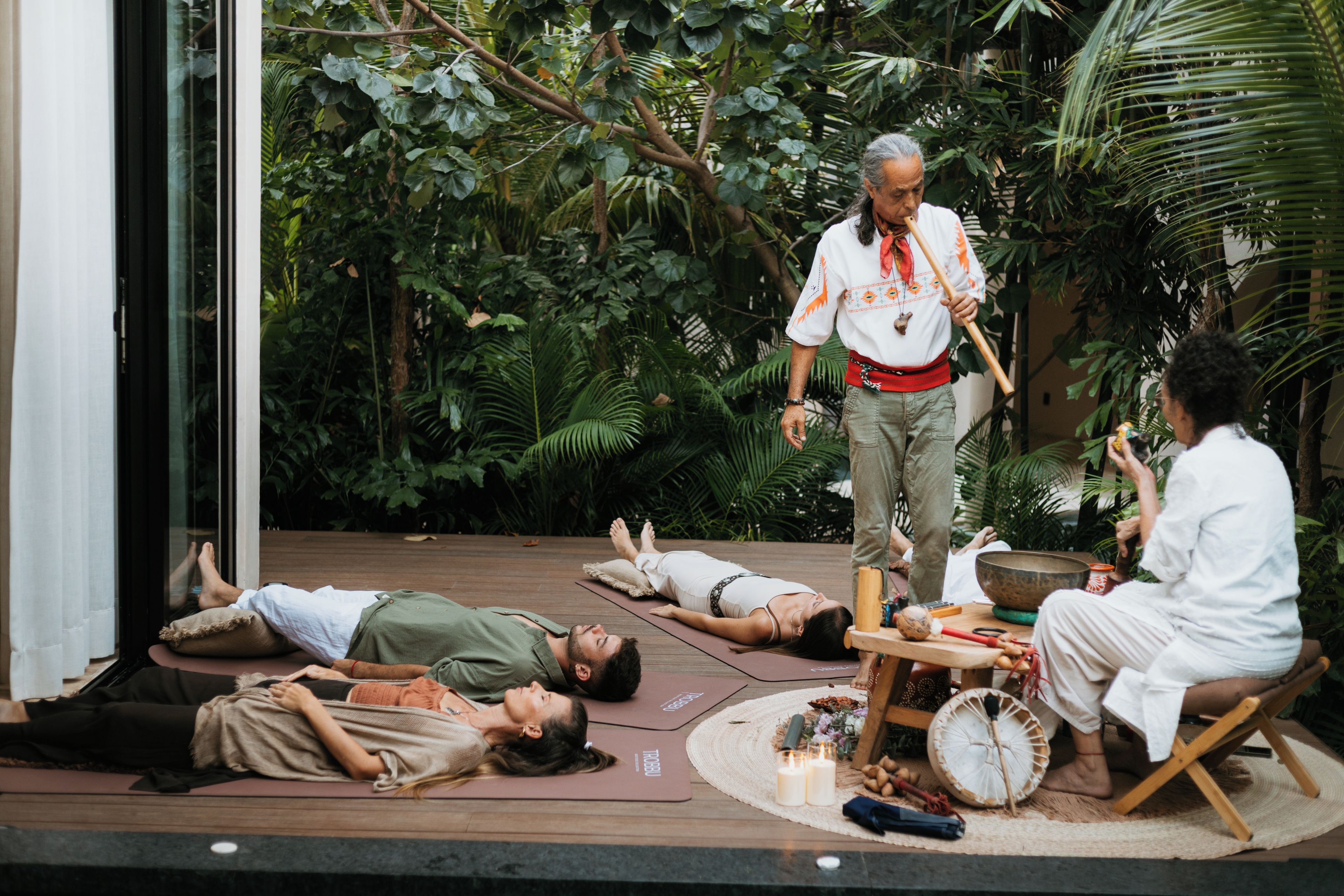 Un grupo de personas practicando yoga al aire libre sobre esterillas, rodeado de exuberante vegetación.