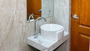 Ein Badezimmer mit einem weißen Waschbecken, einem Spiegel und einer Holztür.