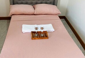 En säng med rosa sängkläder, två handdukar och ett bricka med två glas och en flaska.
