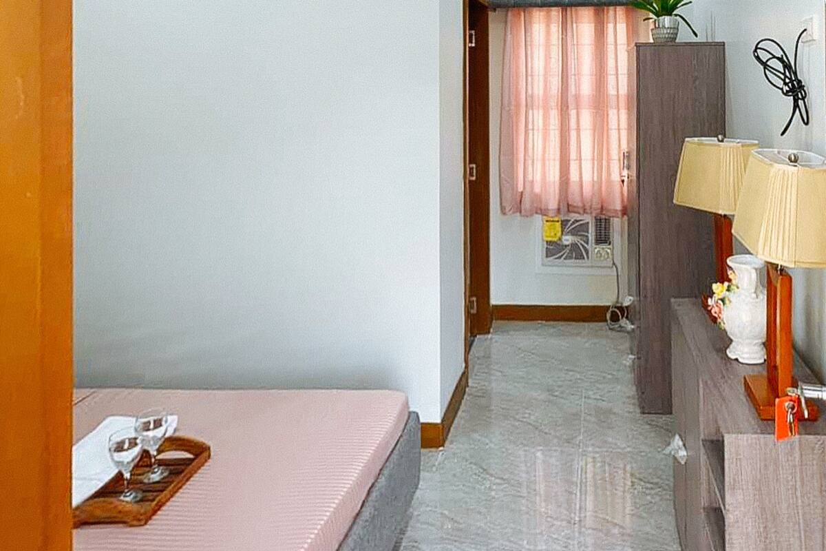 Une chambre d’hôtel avec un lit, un bureau doté d’une lampe, une plante en pot et une fenêtre avec des rideaux.