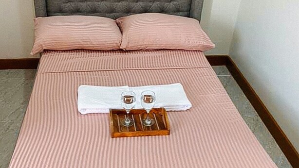 Ein Bett mit rosa Bettwäsche, zwei Handtücher und ein Tablett mit zwei Gläsern und einer Flasche.