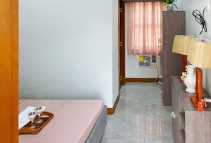 Ett hotellrum med en säng, ett skrivbord med en lampa, en krukväxt och ett fönster med gardiner.