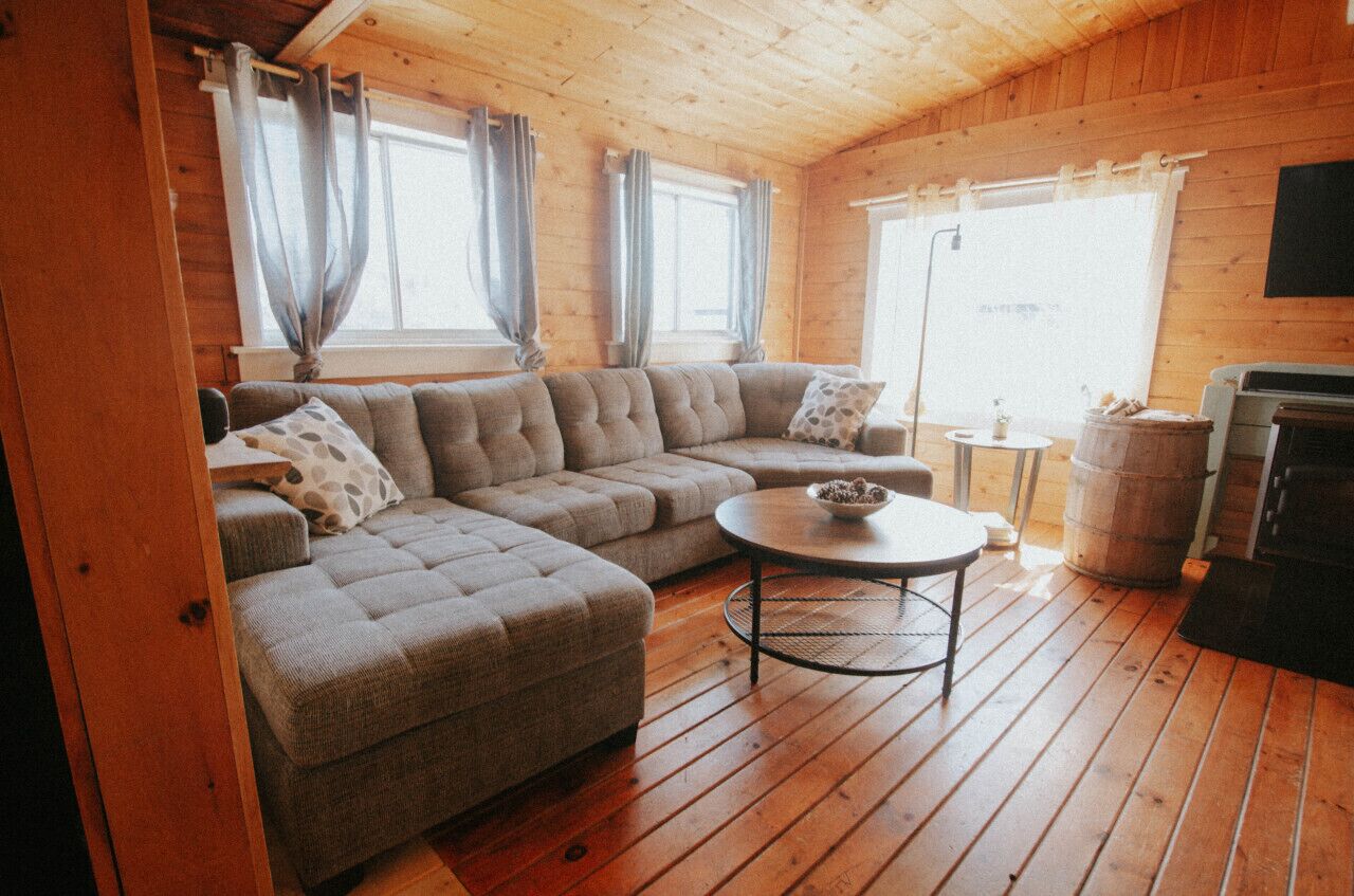 Un intérieur de chalet chaleureux avec un canapé d’angle, une table basse ronde et une cheminée.