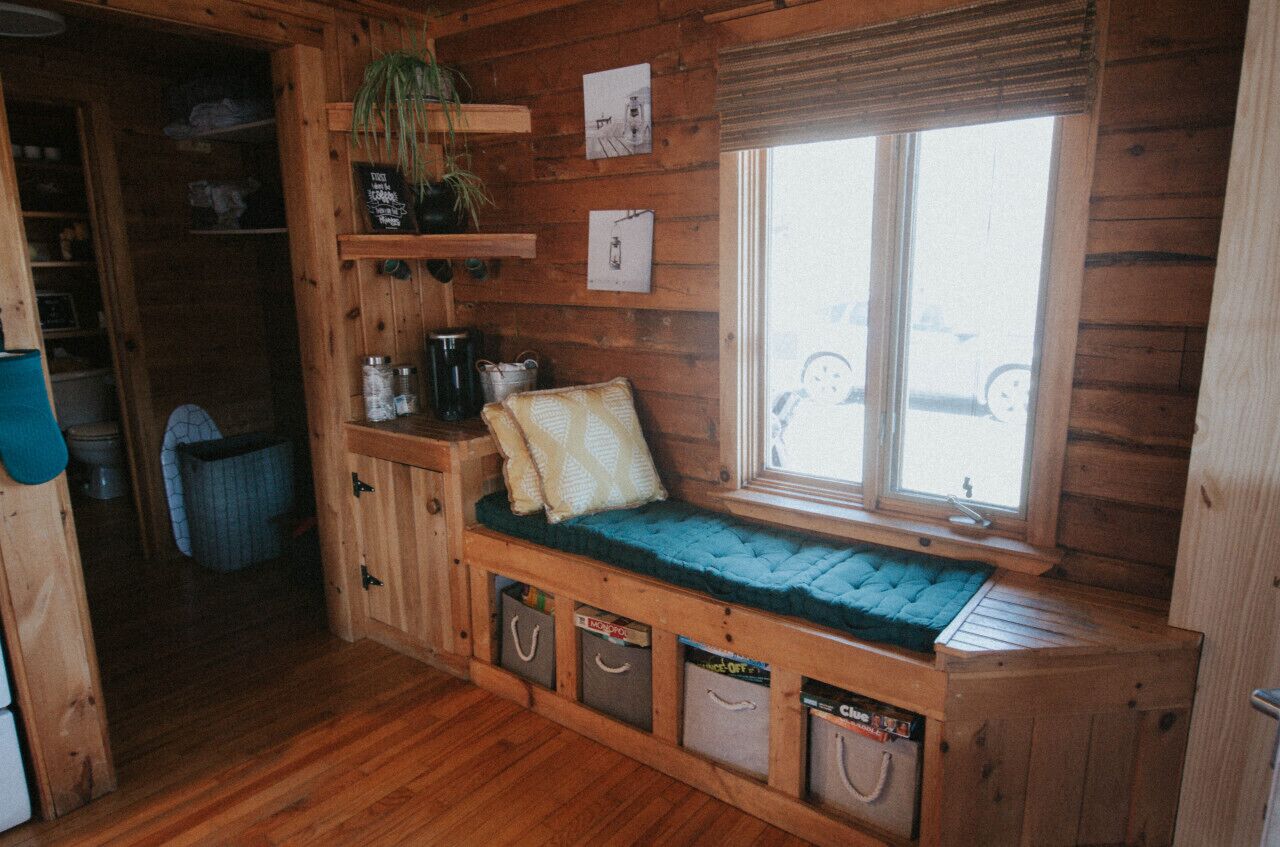 A wooden cabin interior with a built-in bench, shelves, and a window.