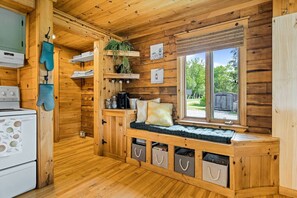 Una cucina accogliente in stile baita, con pareti in legno, una panca integrata con spazio contenitore, una finestra con vista e una pianta pensile.