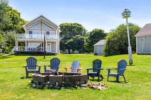 Een tweelaags huis met een balkon, omringd door een gazon met Adirondack-stoelen en een vuurkorf.