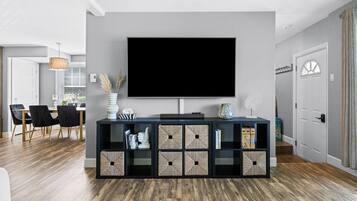 Un soggiorno moderno con una grande TV a schermo piatto, un pavimento in legno scuro e un tavolino consolle minimalista con contenitori.