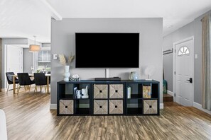 A modern living room with a large flat-screen TV, a dark wood floor, and a minimalist console table with storage boxes.