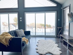 A modern living room with a dark sofa, a white fur rug, and a large sliding glass door leading to an outdoor area.