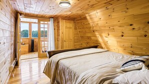 A wooden cabin bedroom with a bed, a window, and a door leading to a balcony.