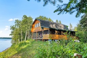 A log cabin with a large deck, surrounded by lush greenery and a lake. - Knotty Pines 4 Bedroom with Waterfront Views (McKinleyville)