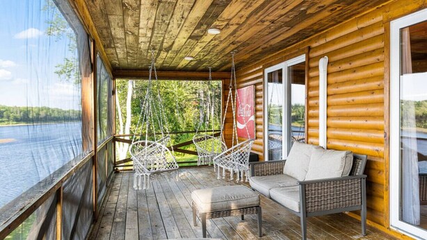 A wooden deck with wicker furniture and a sofa overlooking a lake.