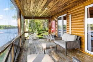 A wooden deck with wicker furniture and a sofa overlooking a lake.