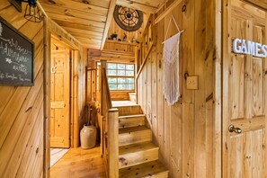 Interior de madera con una escalera, un letrero de bienvenida y una puerta que dice 'GAMES'.