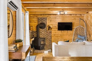 A cozy cabin interior with a fireplace, a hanging chair, a sofa, and a flat-screen TV.