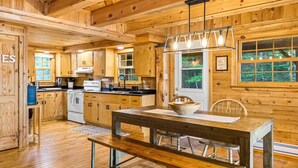 Interior de una cabaña de madera con cocina, mesa de comedor y banco.