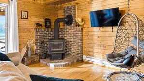 A cozy cabin interior with a brick fireplace, a hanging chair, and a television mounted on the wall.