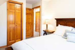 A bedroom with a wooden wardrobe, a bedside table with a lamp, and a bed with pillows. - Get-A-Way Beach Chalet (Grande-Digue)