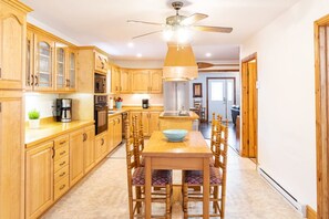 A spacious kitchen with wooden cabinets, a central island, and a dining area with chairs. - Get-A-Way Beach Chalet (Grande-Digue)