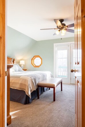 A bedroom with a bed, a bench, a ceiling fan, and a door leading outside.