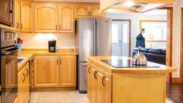 A kitchen with wooden cabinets, a stainless steel refrigerator, and a large island with a kettle.