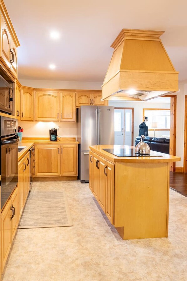 A kitchen with wooden cabinets, a stainless steel refrigerator, and a large island with a kettle. - Get-A-Way Beach Chalet (Grande-Digue)